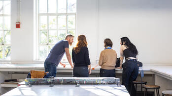 four people standing and talking by a desk with their backs to the camera