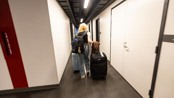 student with luggage walking through a residence hall